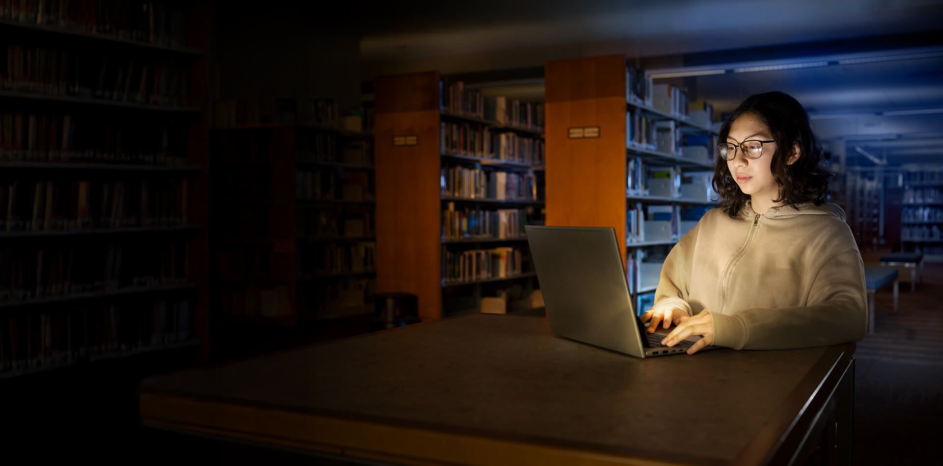 A student sitting in a library at a table doing homework on a laptop.