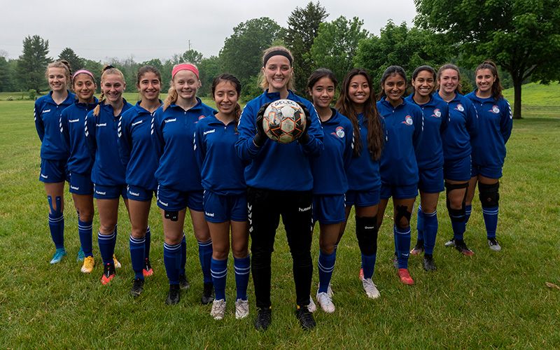 El equipo femenino de ECC alineado con la capitana del equipo sosteniendo un balón de fútbol.