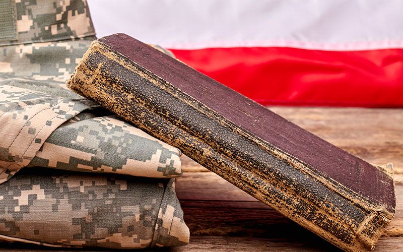 Weathered book resting on a military uniform with an American flag in the background.