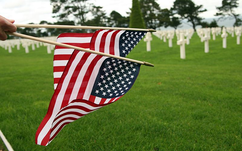 American flags being placed among rows of white grave markers at a military cemetery.