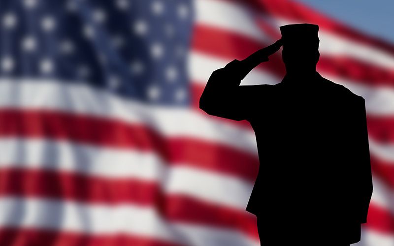 Silhouette of a soldier saluting in front of a large American flag.