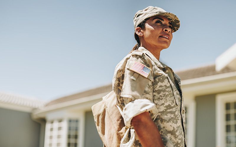 A female service member in uniform standing outdoors with an American flag patch on her sleeve.